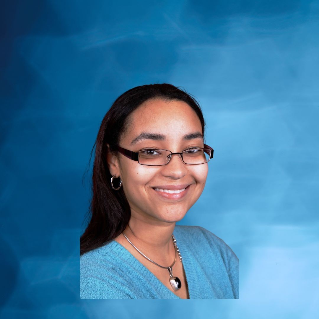 Person wearing a blue sweater and heart-shaped necklace with a blue background.